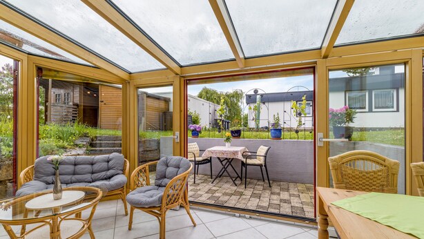 A conservatory with glass doors, wicker furniture, and a tiled patio area. - Holiday Apartment 'Leicht' with Wi-Fi (Münsingen)