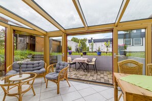 A conservatory with glass doors, wicker furniture, and a tiled patio area. - Holiday Apartment 'Leicht' with Wi-Fi (Münsingen)