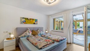 A bedroom with a bed, a nightstand, a painting, a window, and a view of the outside. - Holiday Apartment 'Leicht' with Wi-Fi (Münsingen)