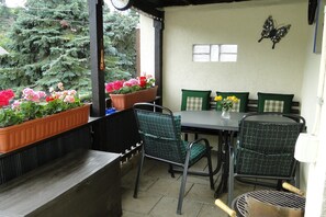 A covered patio with a table and chairs, potted plants, and a butterfly wall decoration.