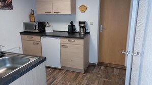 Una cocina compacta con microondas, cafetera y armarios de madera.