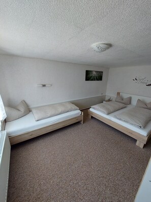 A room with two wooden beds, a small wall-mounted shelf, and a ceiling light fixture.