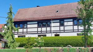 Ein traditionelles Fachwerkhäuschen mit rotem Ziegeldach, einer dahinterliegenden Steinmauer und einer gepflegten Hecke.