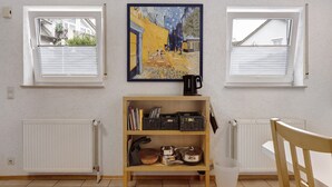 A room with two windows, a radiator, a bookshelf, and a table.