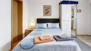 A neatly made bed with a patterned bedspread, a bedside lamp, and a wooden wardrobe.