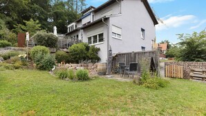 A two-story house with a covered patio, a wooden fence, and a stone wall.