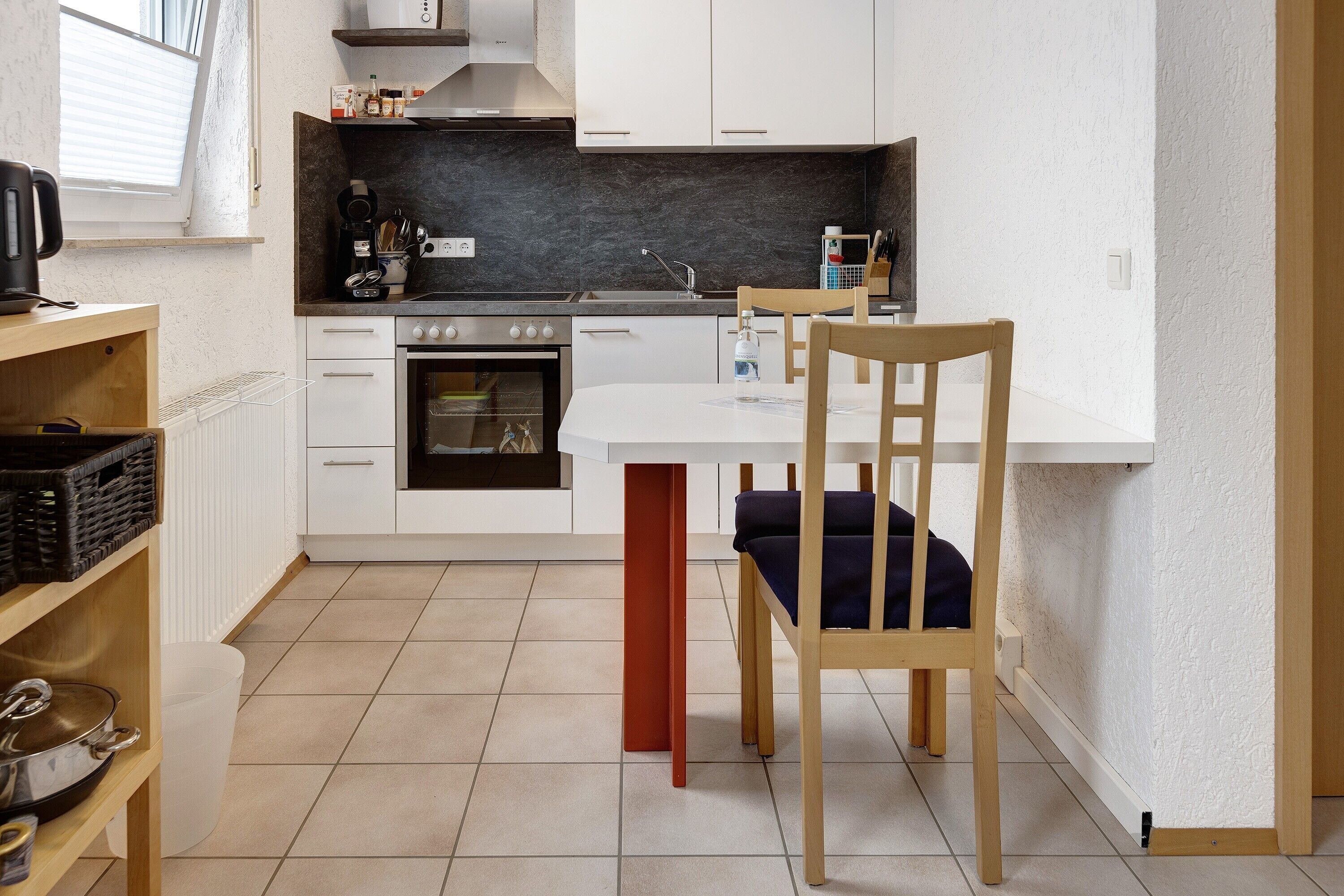 A compact kitchen with white cabinets, a black countertop, and a red support column.