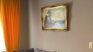 Una sala de estar con sofá, un cuadro, una mesa y una ventana con cortinas.