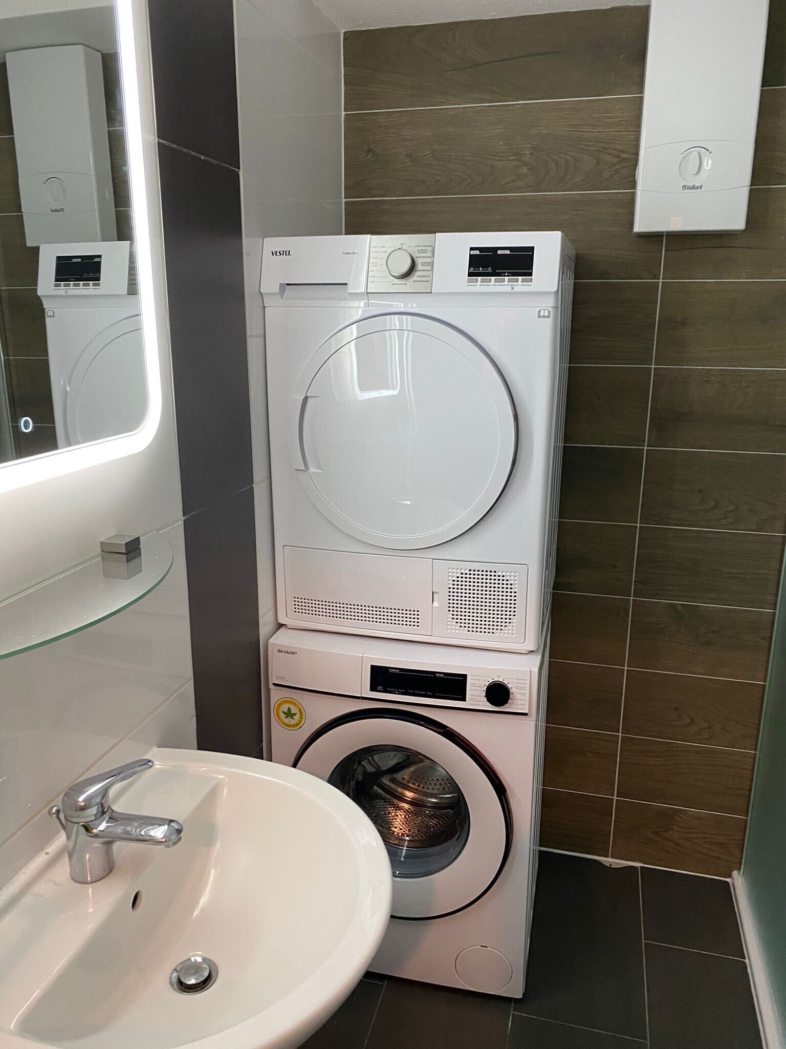 Un bagno compatto e moderno dotato di lavatrice e asciugatrice integrate, lavabo e specchio.