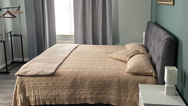 Un dormitorio con cama, mesita de noche, lámpara, un cuadro en la pared y ventana con cortinas.