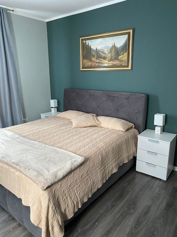 A bedroom with a bed, nightstands, a lamp, a painting, and a window with curtains.