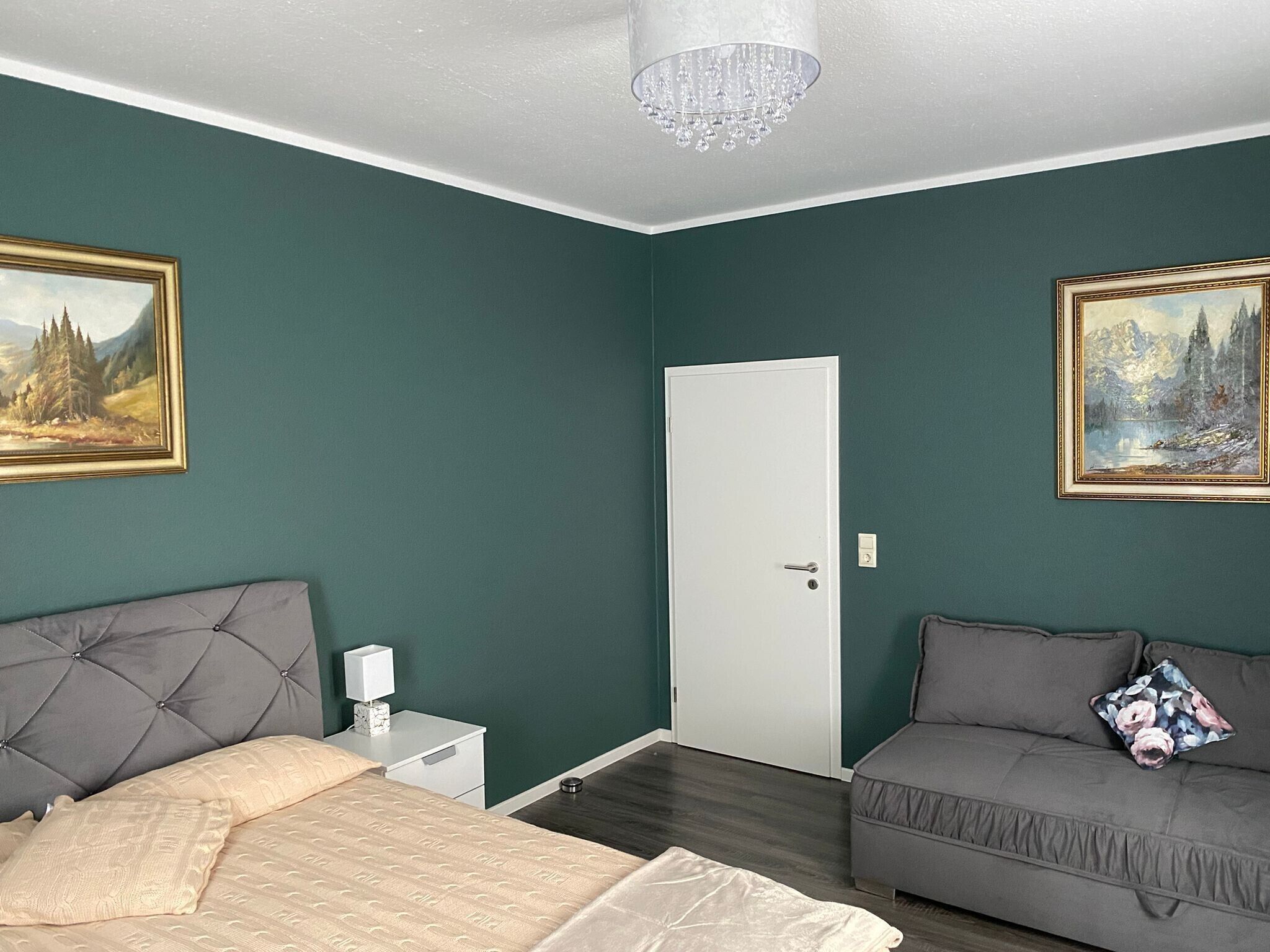 Un dormitorio con cama, sofá, mesita de noche, puerta y dos cuadros en las paredes.
