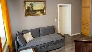 Una sala de estar moderna con un sofá gris, un cuadro con paisaje enmarco, un armario de madera y una silla de mimbre.