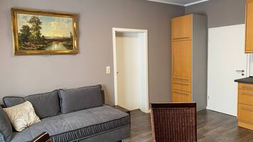 Ett rum med en grå soffa, en tavla, en trägarderob och en fåtölj av rotting.
