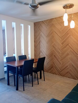 A dining area with a wooden dining table and four chairs, surrounded by a herringbone-patterned wall and a ceiling fan.