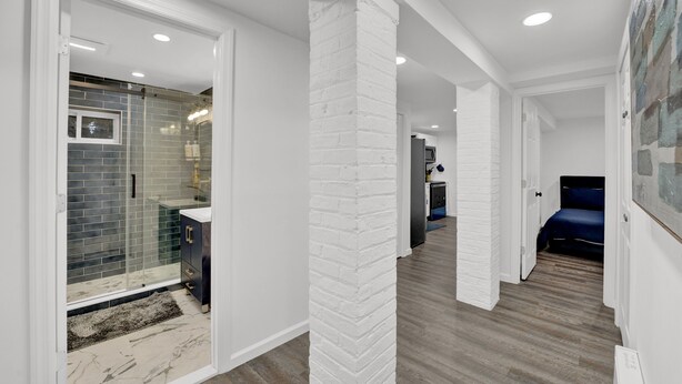 Un interior modern amb dutxa de vidre, columnes de maó blanc i un passadís que condueix a una habitació.