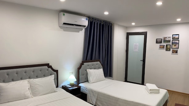 Een hotelkamer met twee bedden, een airconditioner, een nachtkastje met een lamp, een deur met een ruit en lijstjes met foto's aan de muur.