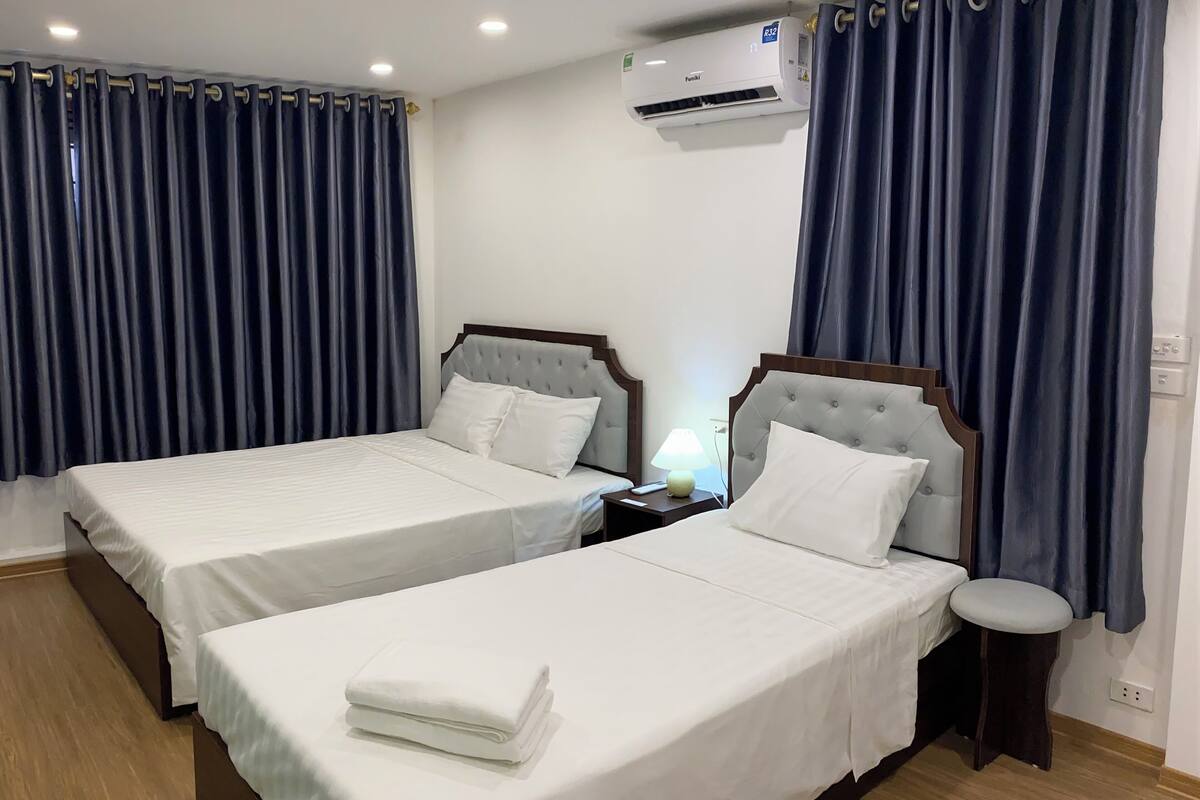 A hotel room with two beds, a nightstand with a lamp, and an air conditioning unit on the wall.