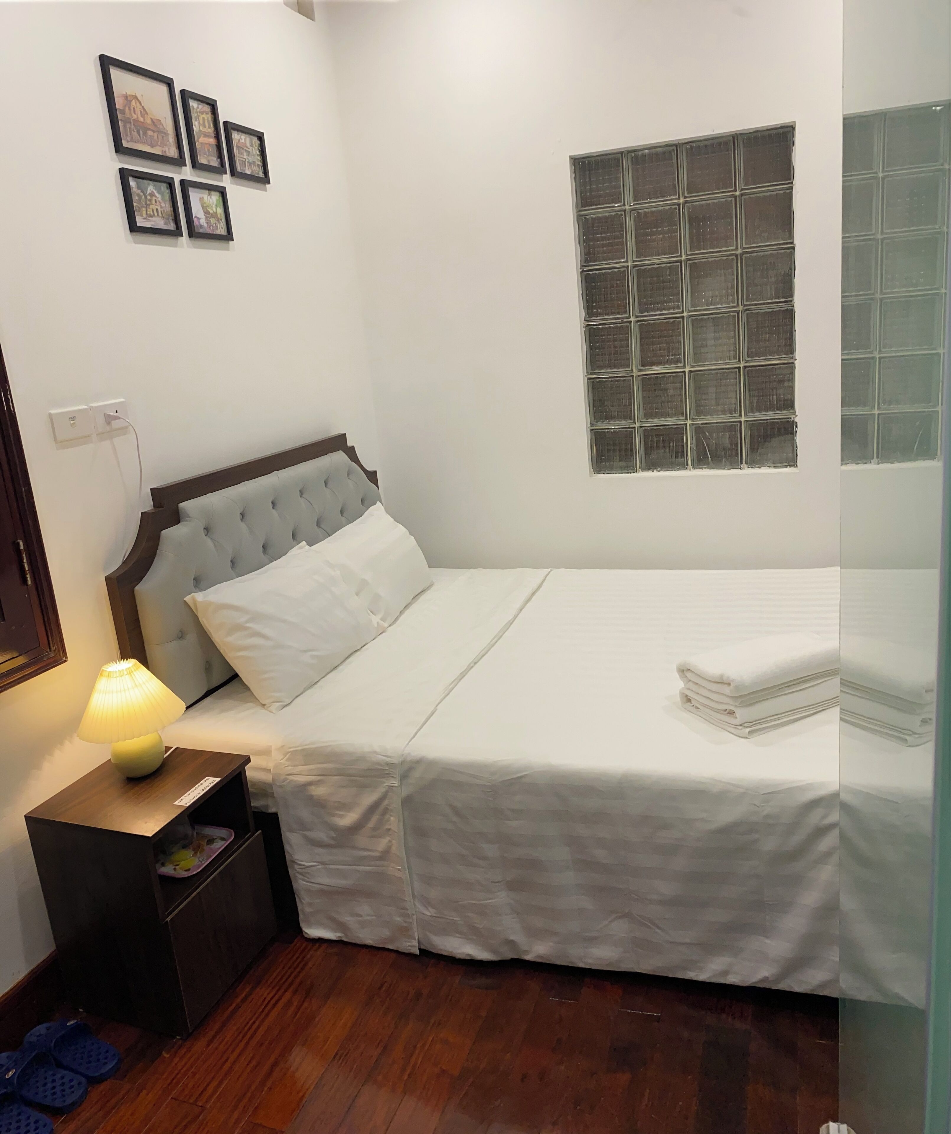 A neatly arranged bedroom with a bed, bedside lamp, and framed pictures on the wall.