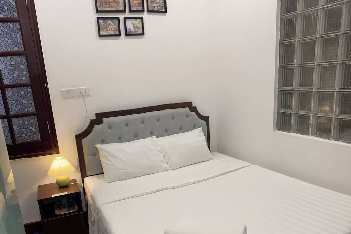 A neatly made bed with white linens, a wooden headboard, and a bedside table with a lamp and a small container.