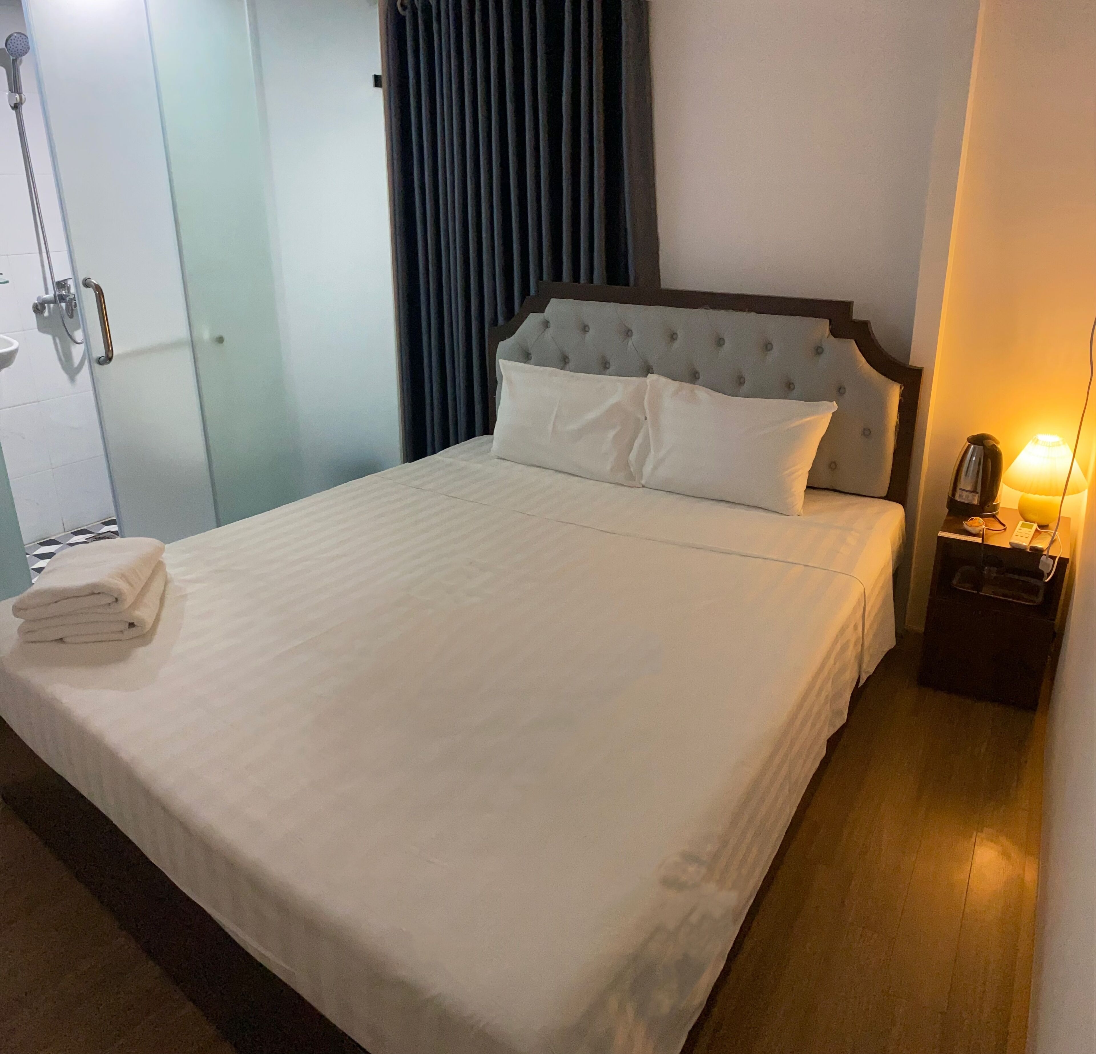 A hotel room with a large bed, a bedside table with a lamp, and a shower area.