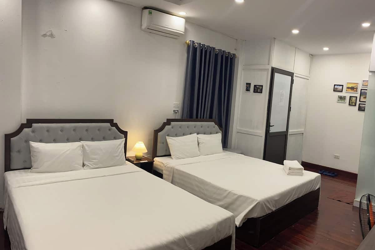 A hotel room with two beds, a ceiling fan, an air conditioning unit, a nightstand with a lamp, a door, and a wall with framed pictures.
