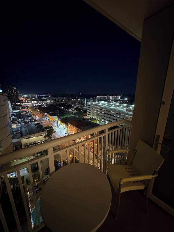 Een balkon met een tafel en stoelen, met uitzicht op een stadsbeeld in de nacht.