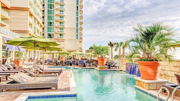 A hotel pool area with lounge chairs, umbrellas, and potted plants. - Luxury Beachfront Resort Studio w/Kitchenette in VA Beach Sleeps 2 (Virginia Beach)