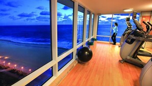 A gym with large windows overlooking a beach at dusk. - Luxury Beachfront Resort Studio w/Kitchenette in VA Beach Sleeps 2 (Virginia Beach)