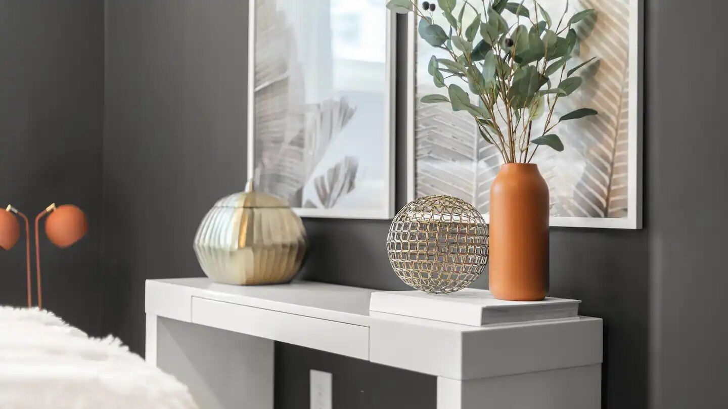 A modern living room with a white console table, a decorative globe, and a vase with green plants.