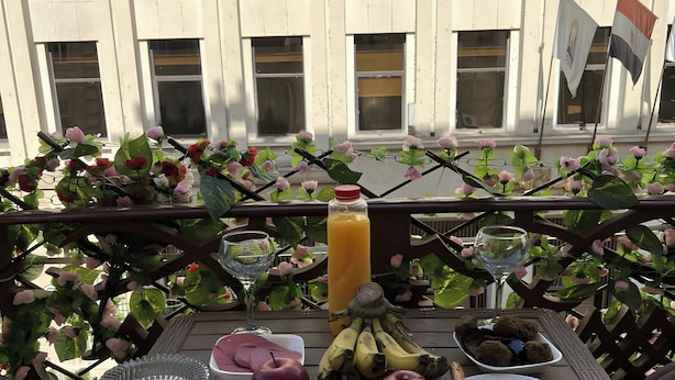 A table set with various foods including bread, apples, bananas, and a bottle of juice, with a view of a building in the background. - Lucky Hostel (Cairo)