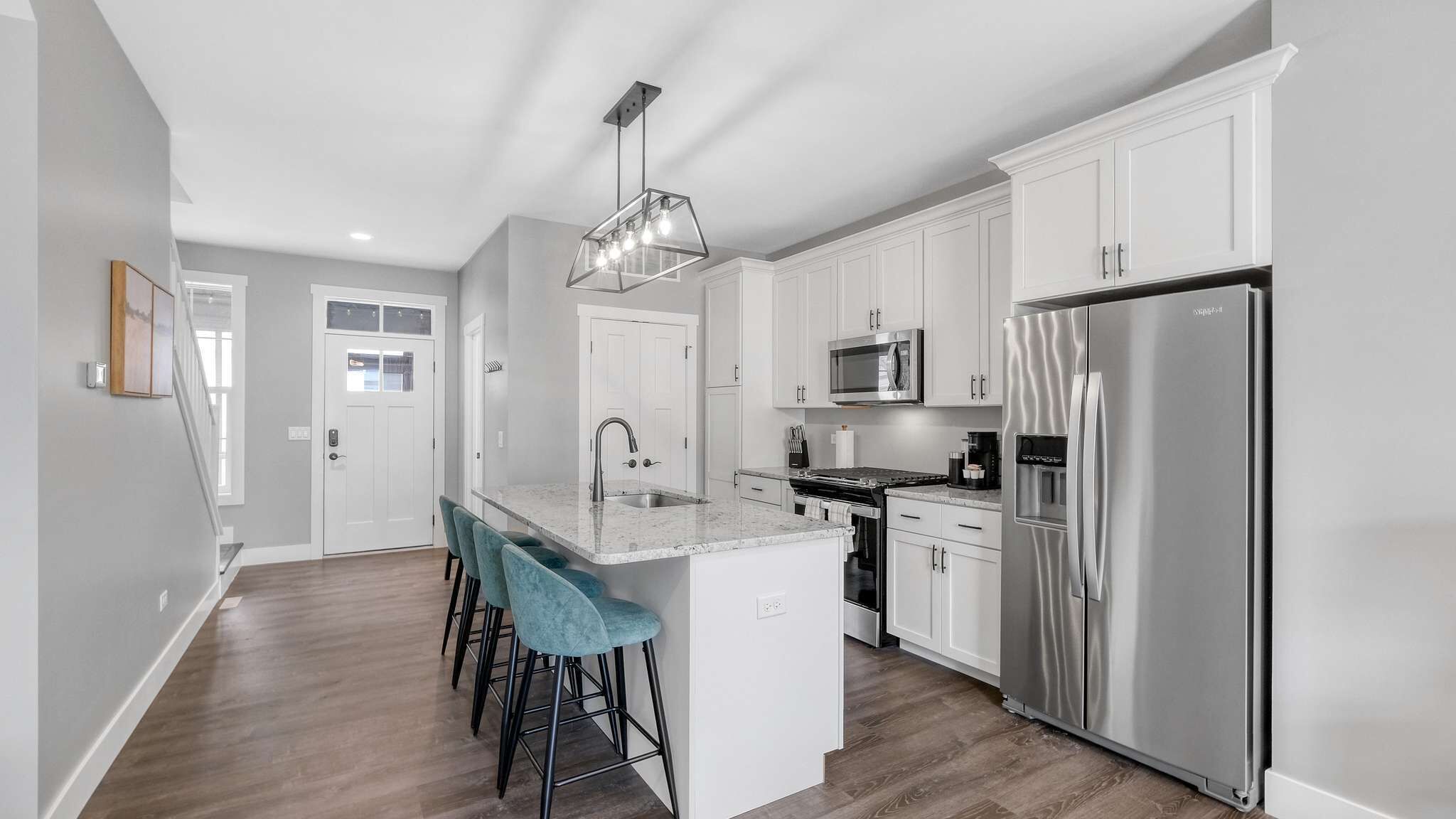 A modern kitchen with white cabinets, stainless steel appliances, a central island with bar stools, and a pendant light.