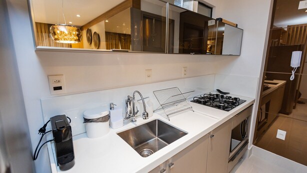 Una cocina moderna con un lavamanos de acero inoxidable, una estufa a gas y un horno empotrado. Hay un espejo sobre el lavamanos y una lámpara colgante.