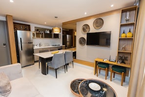 A modern kitchen with a dining area, a TV mounted on the wall, and a small seating area with a table and chairs. - Fortune Cabo Branco (João Pessoa)