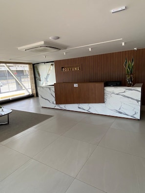 A modern reception desk with a marble top and wooden paneling, labeled "FORTUNE." - Fortune Cabo Branco (João Pessoa)