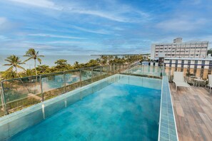 A rooftop infinity pool with a glass barrier, overlooking a beach and palm trees. - Fortune Cabo Branco (João Pessoa)