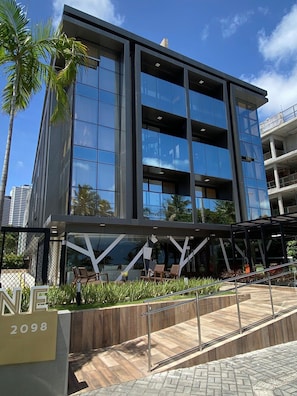 A modern building with a glass facade, a covered outdoor seating area, and a visible entrance. - Fortune Cabo Branco (João Pessoa)