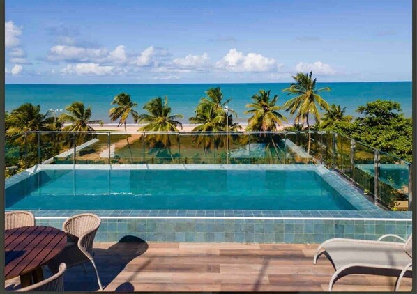 A pool with a view of the beach and palm trees.
