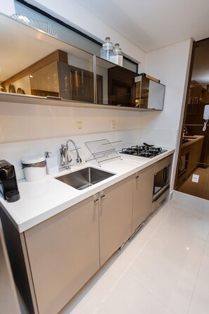 A modern kitchen with a white countertop, stainless steel sink, and a gas stove. - Fortune Cabo Branco (João Pessoa)