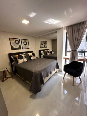 A modern bedroom with a large bed, a side table, and a chair. - Fortune Cabo Branco (João Pessoa)