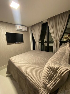 Una habitación de hotel con cama, cortinas, televisor montado y aire acondicionado.