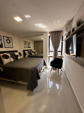 A modern bedroom with two beds, a flat-screen TV, and a large window with curtains.