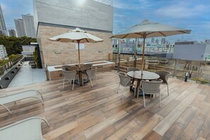 Um pátio externo com piso de madeira, cadeiras de vime e guarda-sóis.