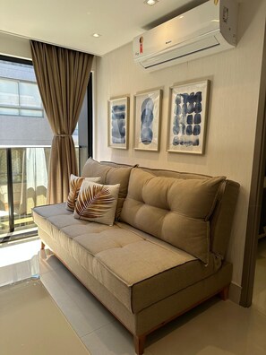A modern living room with a beige sofa, a large window with curtains, and three framed abstract artworks on the wall. - Fortune Cabo Branco (João Pessoa)