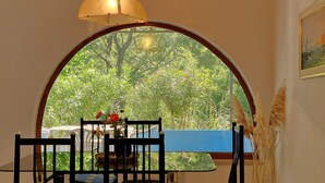 Un comedor con una mesa, sillas, un jarrón con flores y vistas a través de un ventanal arqueado.