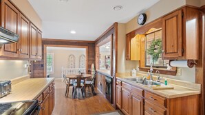 A kitchen with wooden cabinets, a dining table with chairs, and a clock on the wall. - Carols Cottage - Double decker dock! Popular location! (Cullman)