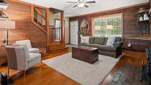 A living room with wooden walls, a ceiling fan, a sofa, a coffee table, and a staircase. - Carols Cottage - Double decker dock! Popular location! (Cullman)