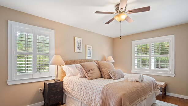 A bedroom with a bed, two bedside tables, a ceiling fan, and two windows with blinds. - Carols Cottage - Double decker dock! Popular location! (Cullman)
