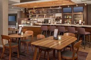 Eine moderne Bar mit Holztischen und -stühlen, einer Theke mit Speisekarte und einer mit Flaschen gefüllten Bar.
