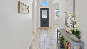 A hallway with a wooden sign reading "FAMILY," a black door with a window above it, and a potted orchid on a console table.